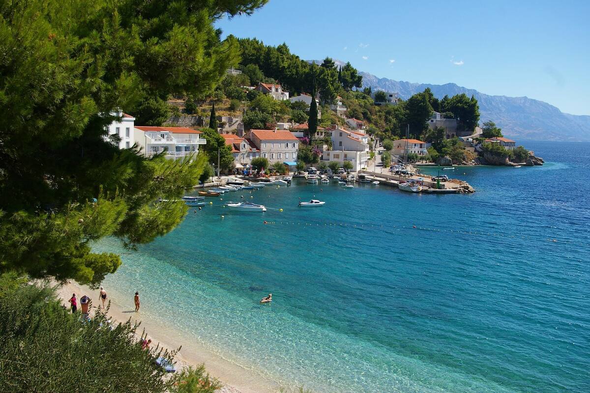 A coastal town with clear waters, a beach, and buildings on a hillside.