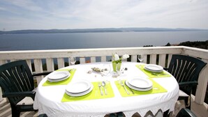 A round table set for four with white plates, silverware, and a vase of flowers, overlooking a body of water. - Apartments Vesna Mimice (Omis)