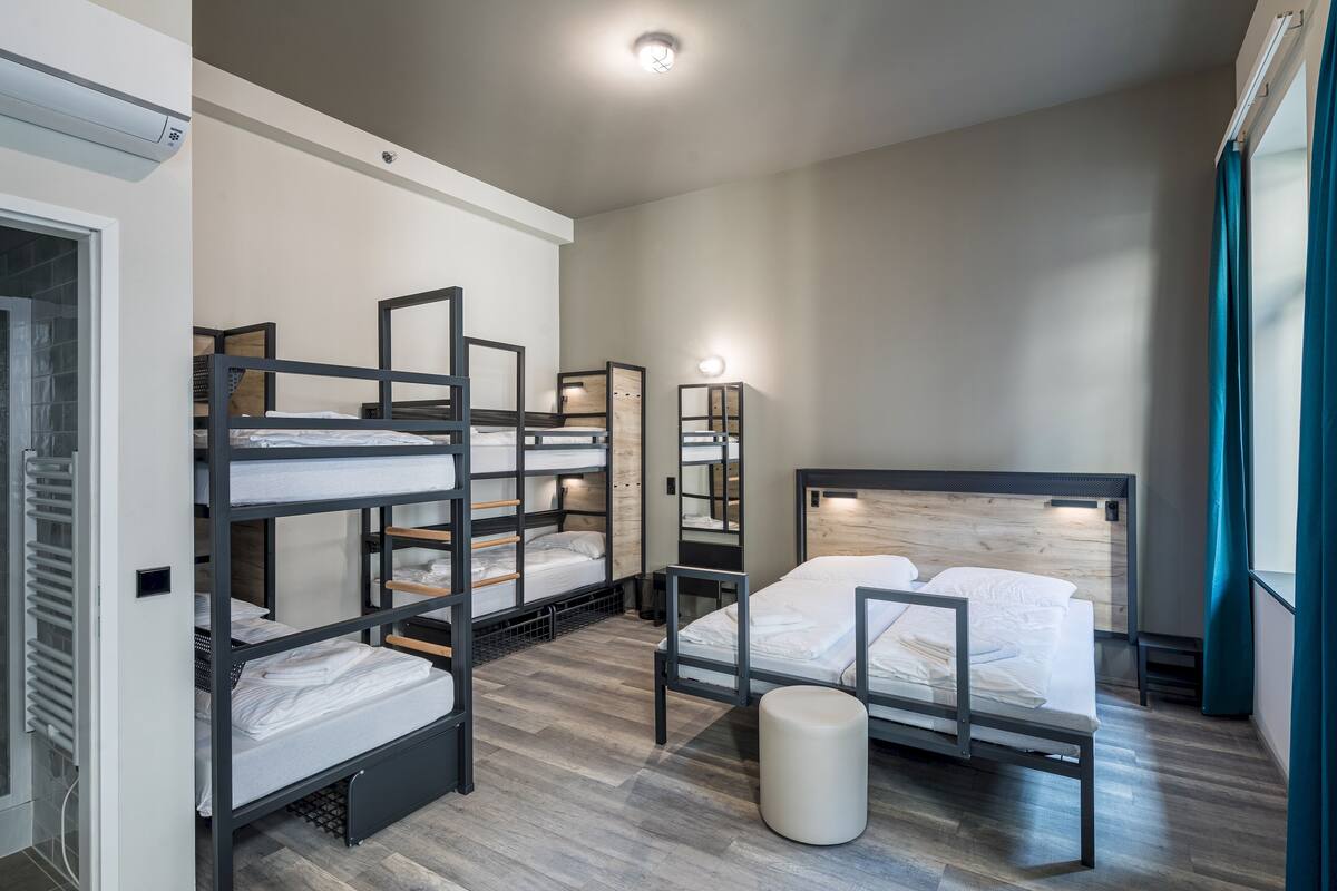 A hotel room with bunk beds, a single bed, a round stool, and a mirror.