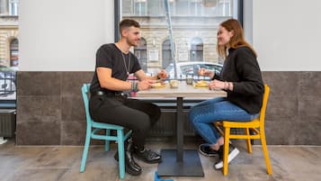 Two people sitting at a table in a cafe with a view of a building through the window.