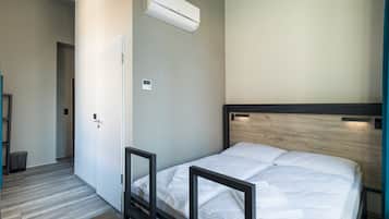 A bedroom with a bed, a door, an air conditioning unit, and a small bedside table.