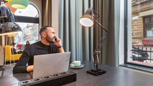 A man sitting at a table with a laptop, a cup, and a lamp. - a&o Budapest City - Hostel (Budapest)