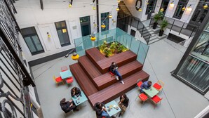 An indoor atrium with a central seating area, glass railings, and multiple tables and chairs. - a&o Budapest City - Hostel (Budapest)