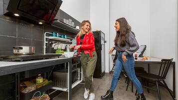 Cocina moderna con electrodomésticos de acero inoxidable, microondas y refrigerador. Cuenta con una mesa de comedor con sillas y una pequeña encimera con pileta e hervidor.