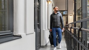A man walking on a corridor with a railing, a light fixture, and a door with a metal gate. - a&o Budapest City - Hostel (Budapest)