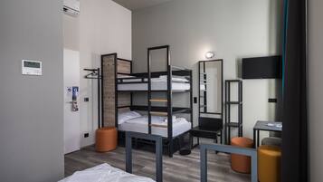 A compact hotel room with bunk beds, a desk, a chair, a small table, a TV, and a mirror.