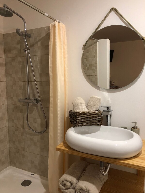 A bathroom with a shower, a sink, a mirror, and towels. - Terra Luso (Cadaval)
