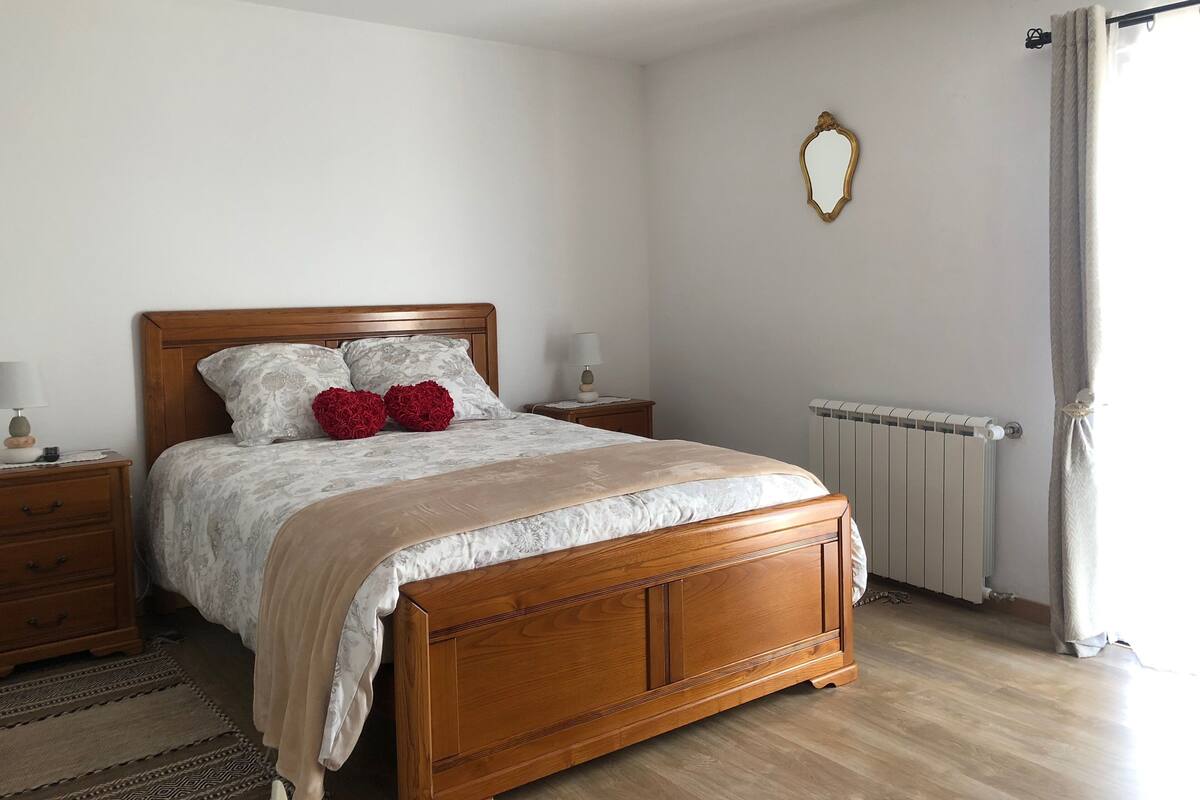 A bedroom with a wooden bed, two bedside tables, a radiator, and a window with curtains.