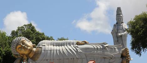 A large reclining statue with a golden head and a white body, surrounded by a red-roofed structure.