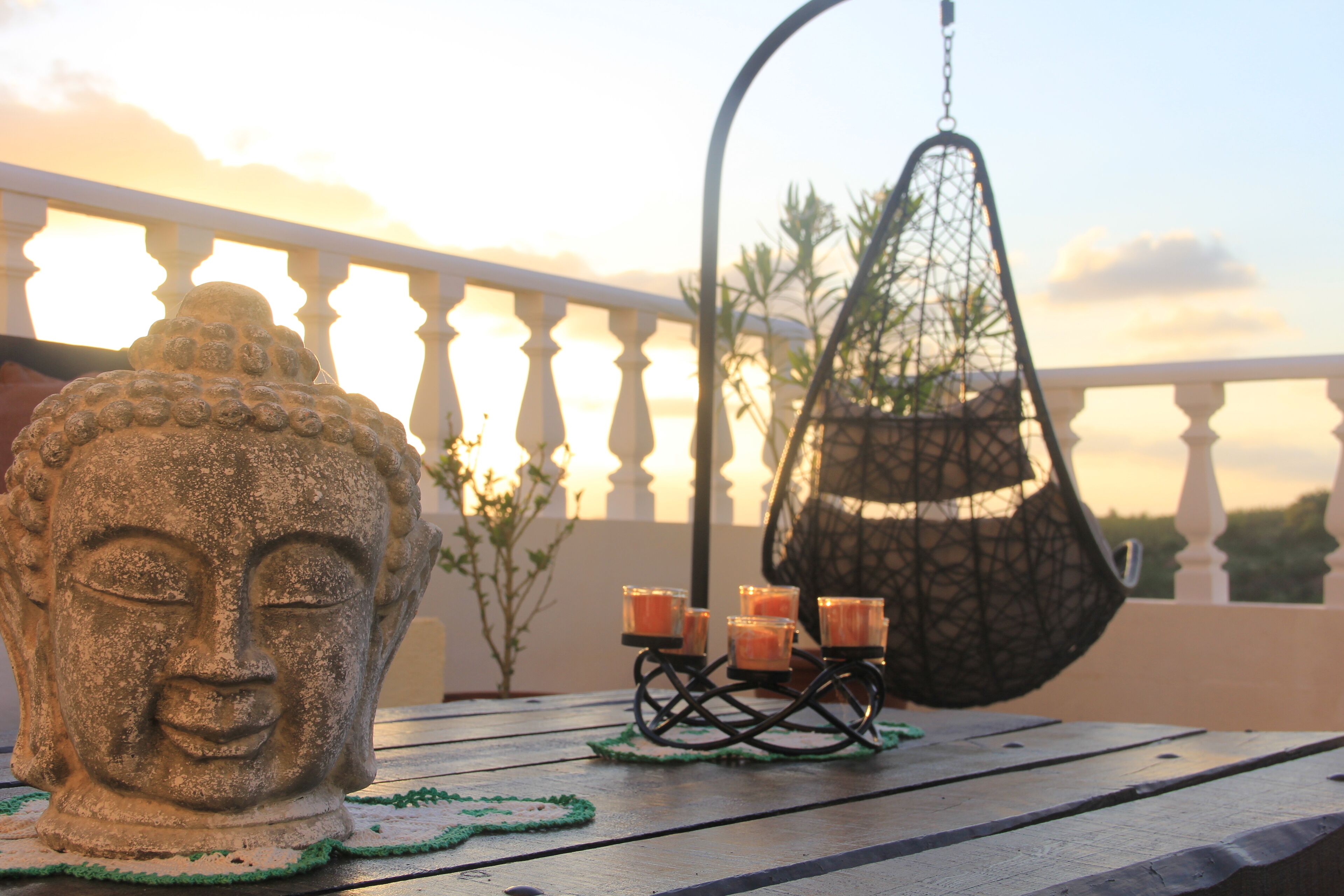 Una escultura de cabeza de Buda, un sillón colgante y velas en un balcón.