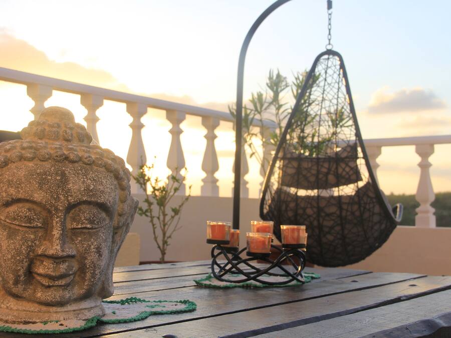 Una escultura de cabeza de Buda, un sillón colgante y velas en un balcón.