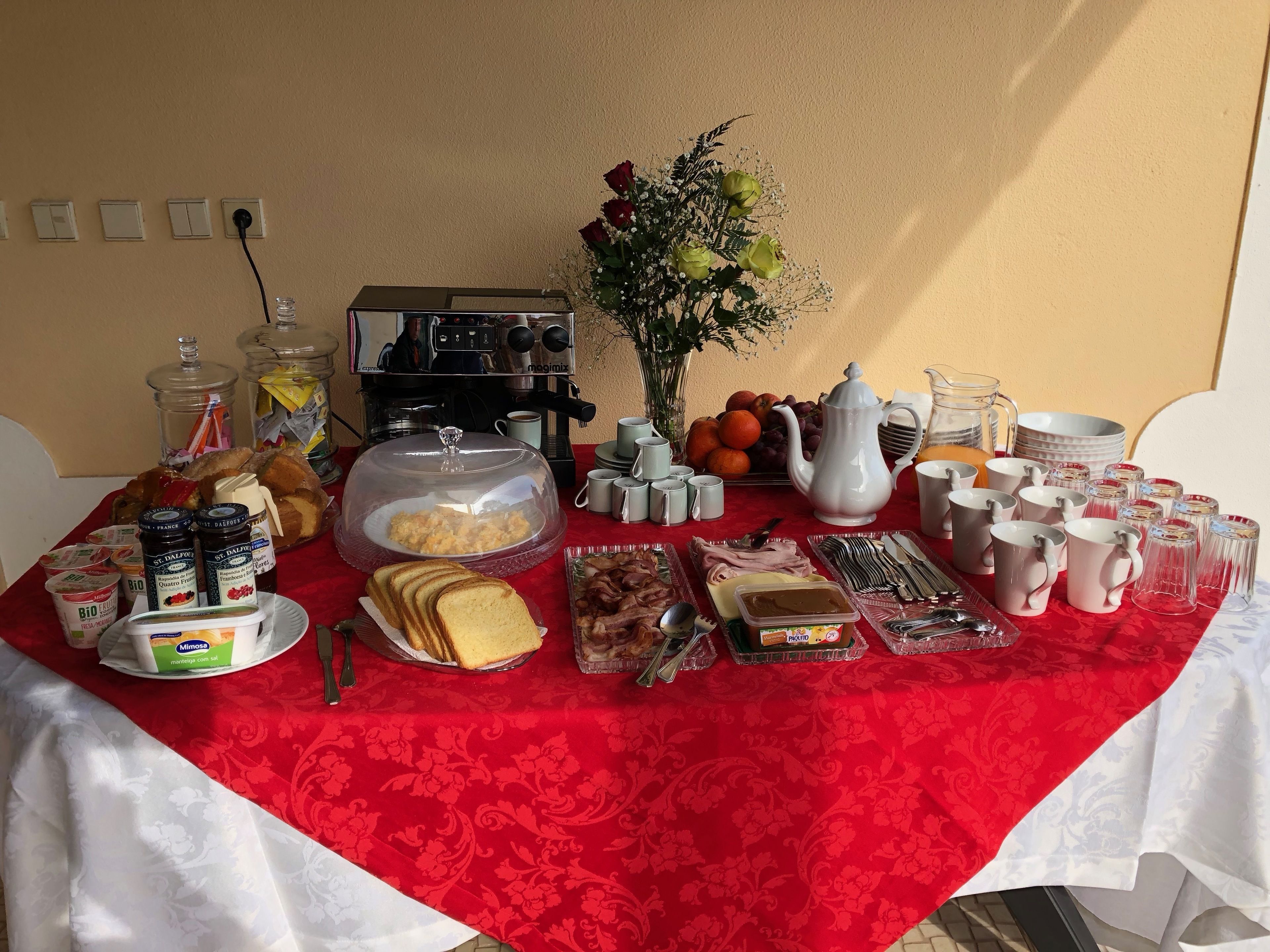 A breakfast buffet with various food items, a coffee machine, and a vase with flowers.