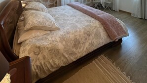 Un dormitori amb paret de pedra simulada, un llit amb roba de llit floral, un televisor fixat a la paret i una finestra amb cortines.