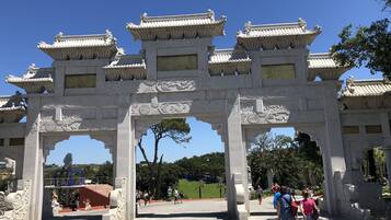 A traditional gate with intricate carvings and multiple tiers, leading to a park area with visitors.