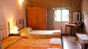 A room with two beds, a wooden wardrobe, a small table with a mirror, and a window with decorative shutters. - Ristoro Del Cavaliere (Piazza al Serchio)