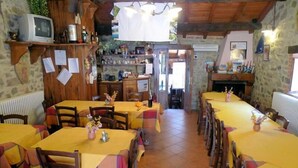 A rustic dining area with wooden tables and chairs, a television on a shelf, and a fireplace. - Ristoro Del Cavaliere (Piazza al Serchio)