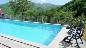 A swimming pool with a metal railing, surrounded by greenery and hills. - Ristoro Del Cavaliere (Piazza al Serchio)