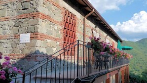 A stone building with a balcony, a metal railing, and pink flowers. - Ristoro Del Cavaliere (Piazza al Serchio)