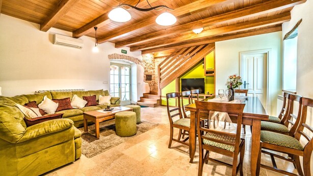 Un vaste espace de vie avec un canapé vert, une table à manger en bois et des chaises. Un escalier mène à un niveau supérieur.