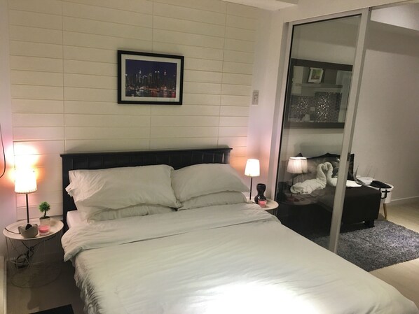Ein Hotelzimmer mit einem Bett, zwei Nachttischlampen, einem gerahmten Bild an der Wand und einer Glastrennwand mit Spiegelung.