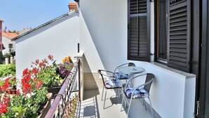 A balcony with a table and chairs, a window with shutters, and potted plants. - Apartment Suki / Three Bedrooms (Rovinj)