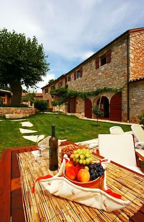 A stone building with a garden, outdoor seating, and a table with fruit and a bottle.