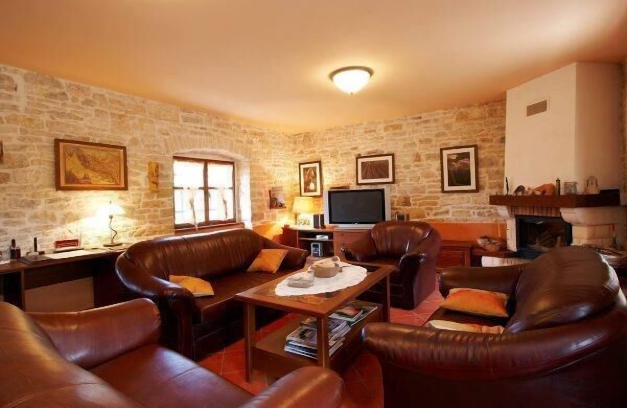 A cozy living room with stone walls, leather sofas, a wooden coffee table, and a fireplace.
