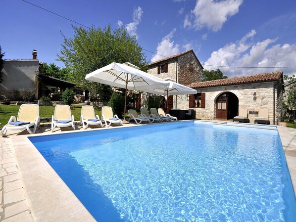 A swimming pool with lounge chairs and umbrellas, surrounded by stone buildings and greenery.