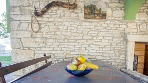 Un mur de pierres, un banc en bois rustique et une table recouverte d’une nappe à motifs floraux.