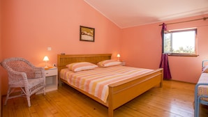 Une chambre à coucher avec un lit en bois, une chaise en osier, une table de chevet avec une lampe et une fenêtre avec des rideaux.