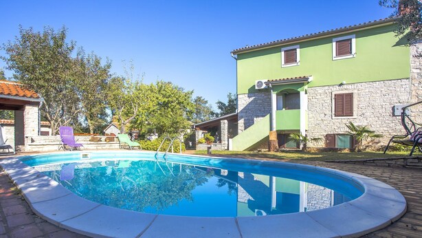 Une piscine bordée de pierres, entourée d’une terrasse dallée.