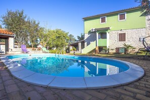Une piscine bordée de pierres, entourée d’une terrasse dallée.