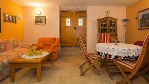 Un salon chaleureux avec un canapé, une table en bois et une table à manger avec des chaises. On y trouve également un meuble en bois doté de portes en verre et une lampe.