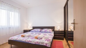 Un lit bien fait, avec une literie à motifs floraux, deux tables de chevet avec des lampes, un tapis rouge et un grand miroir au mur.