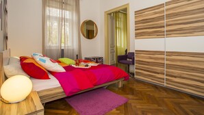 Een slaapkamer met een bed, nachtkastje, spiegel, kledingkast en een deur naar een andere kamer.