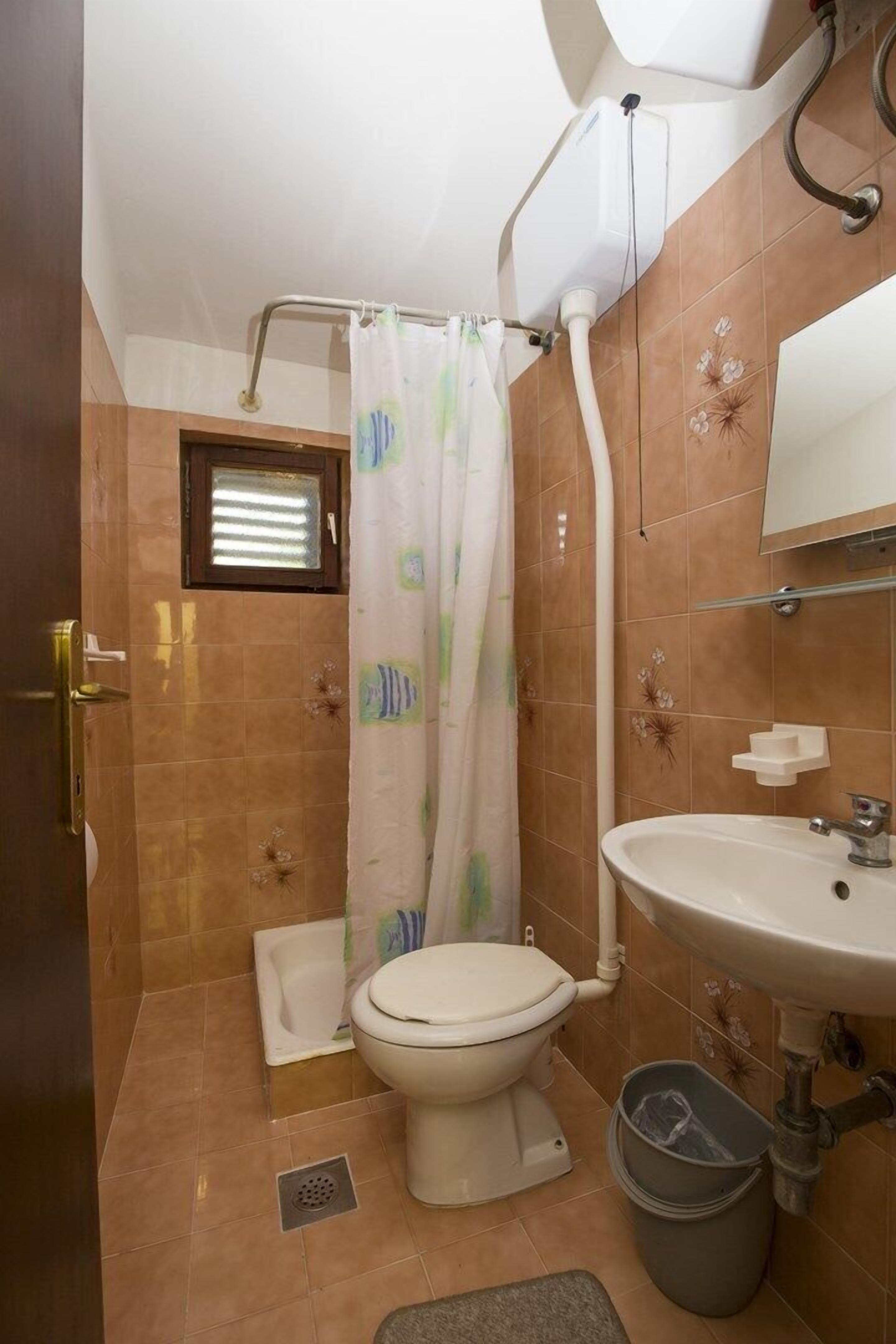 A bathroom with a toilet, sink, shower curtain, and a small window.