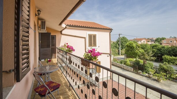 A balcony with a table and chairs, a small potted plant, and a view of a residential area.