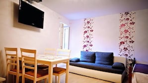 A living room with a sofa, a TV mounted on the wall, and a dining area with a table and chairs. - Studio Erika (Rovinj)