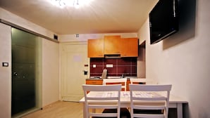 A compact kitchen with wooden cabinets, a white table with chairs, and a flat-screen TV mounted on the wall. - Studio Erika (Rovinj)