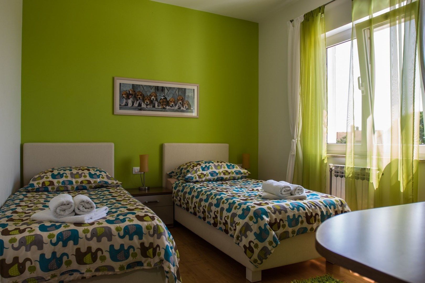 A hotel room with two beds, green walls, a framed picture on the wall, and a window with curtains.