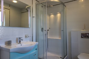 A modern bathroom with a glass-enclosed shower, a white sink with a blue cabinet, and a large mirror above the sink.