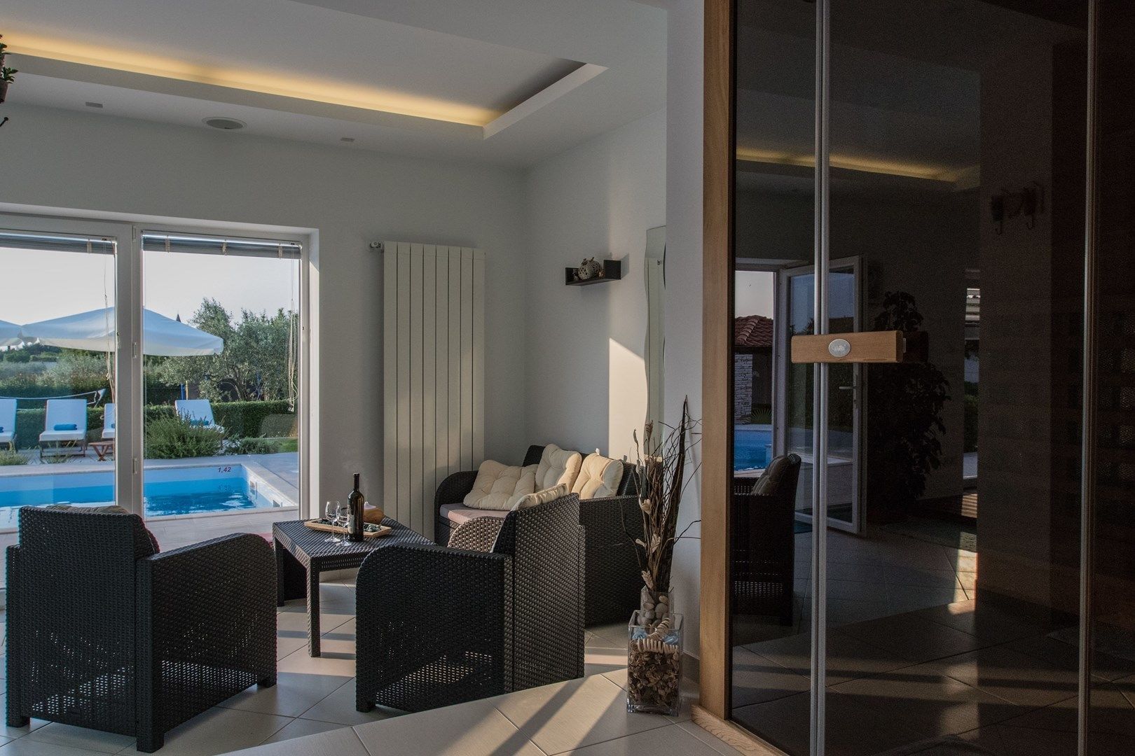 Un salón moderno con vista a la piscina, muebles de mimbre y un ventanal que da a otra habitación.