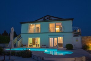 A two-story house with a swimming pool, balconies, and a stone wall.