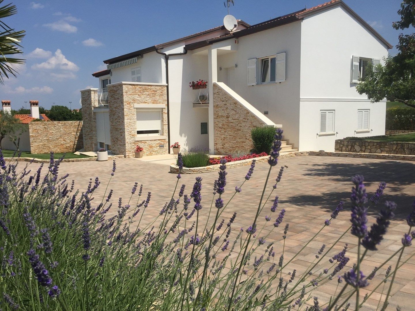 Ein zweistöckiges Haus mit einer Stein-Fassade, ein kleiner Vorgarten mit Lavendel und ein klarer Himmel.