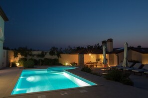 A swimming pool with a curved design, a patio area with lounge chairs, and a building with a tiled roof.