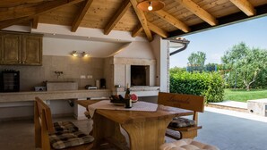 A rustic outdoor kitchen with a stone countertop, wooden chairs, and a table set for dining. - Istrian Villa Lavanda (Kanfanar)