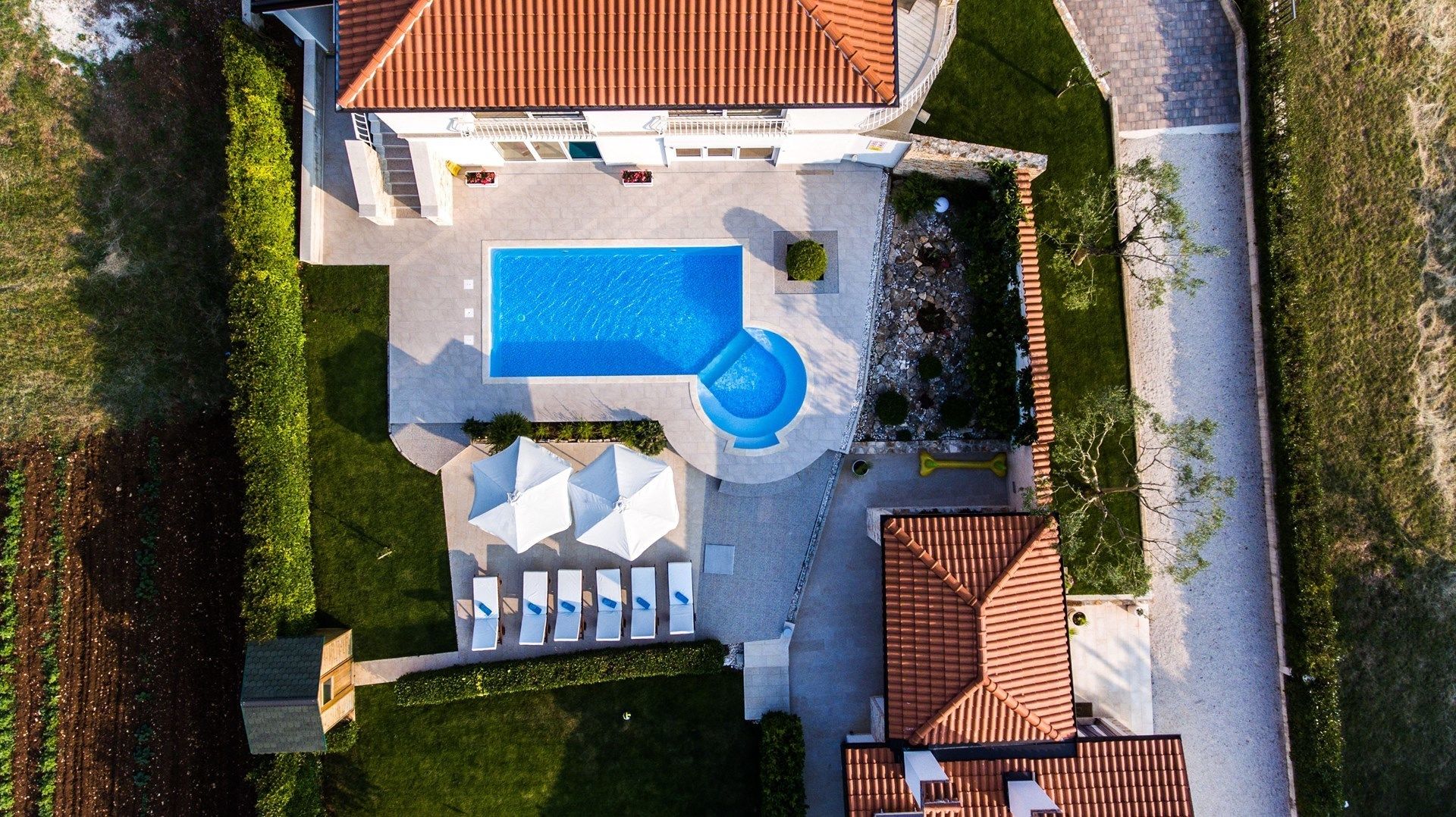 An aerial view of a residential property with a swimming pool, a covered patio area, and a landscaped garden.