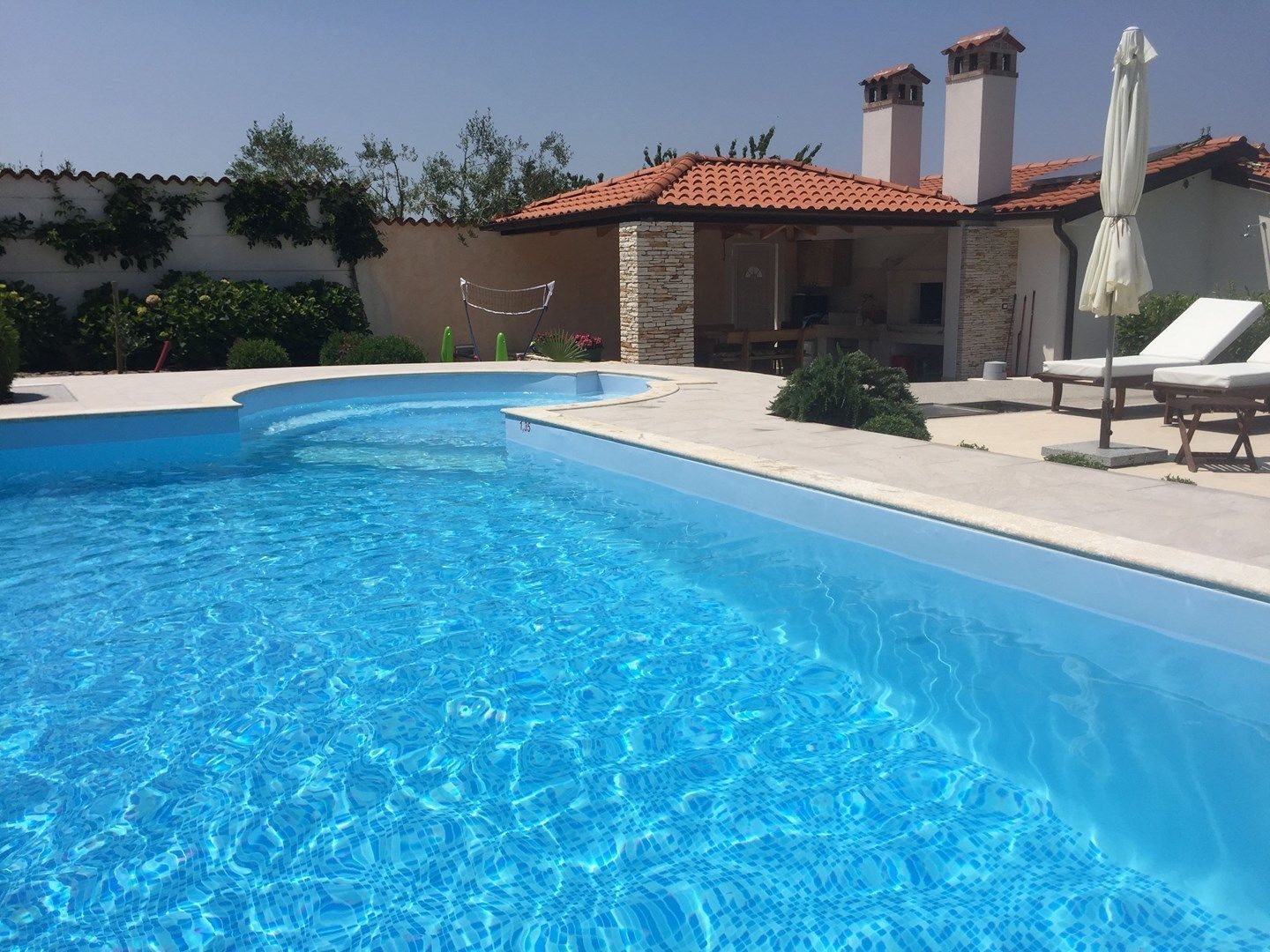 A clear blue swimming pool with a stone and brick house in the background.
