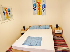 Une chambre à coucher avec un lit, deux tables de chevet, une lampe sur chacune, un coussin à motifs et un tapis coloré.