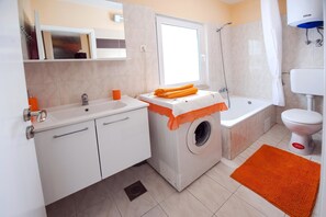 A compact bathroom with a washing machine, a bathtub, and a toilet. - Apartment Tomy / Studio A2 (Rovinj)